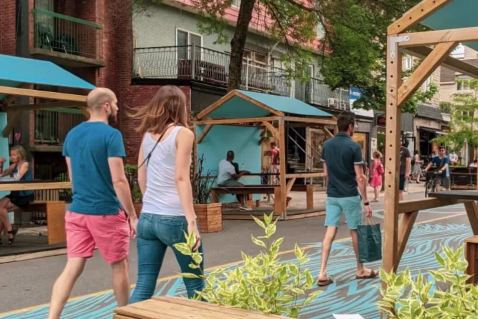Pedestrians walk down car-free Mont-Royal Avenue next to green outdoor dining kiosks in Montreal, Canada